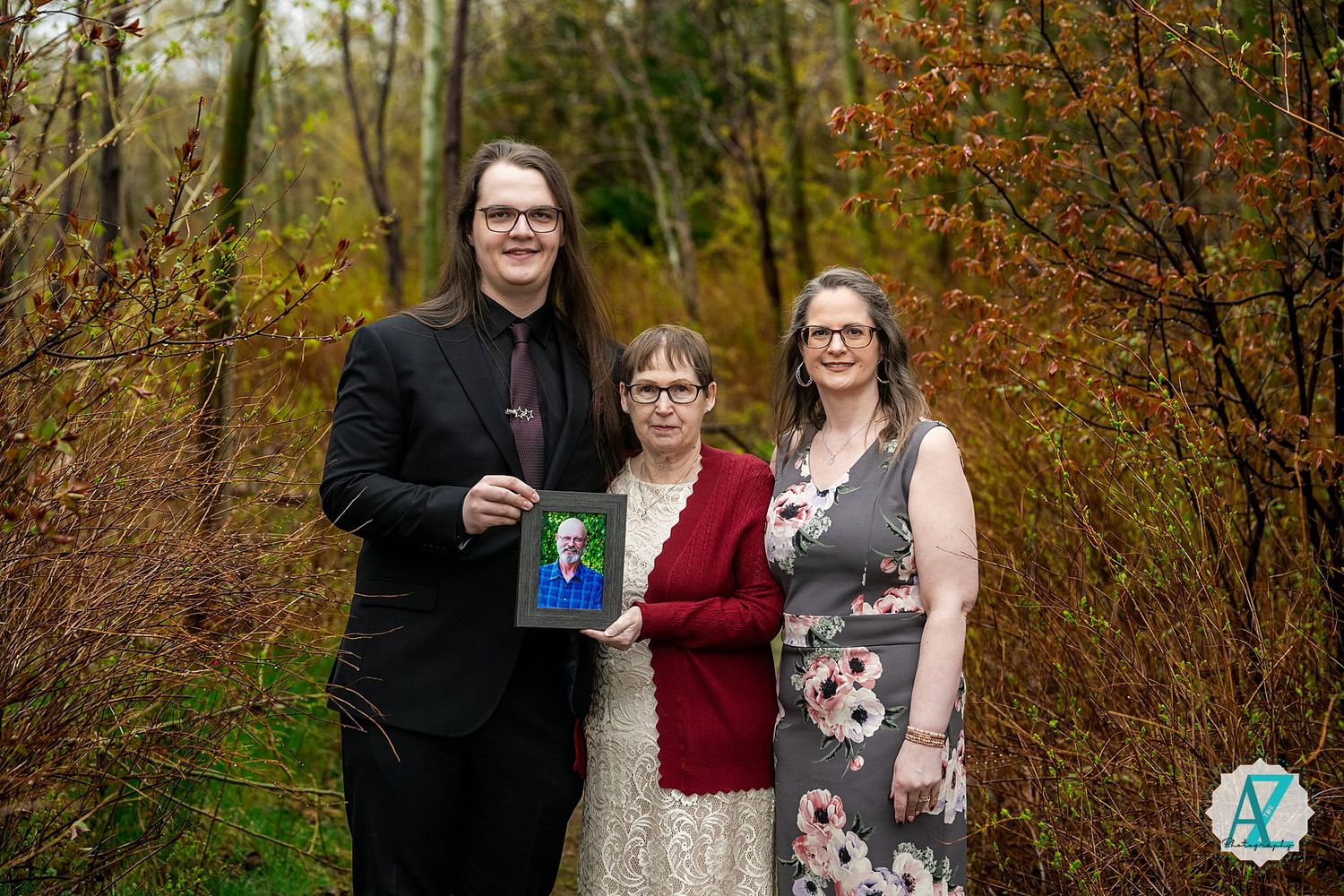 Three people stand together in a forest setting during autumn while holding a small book.