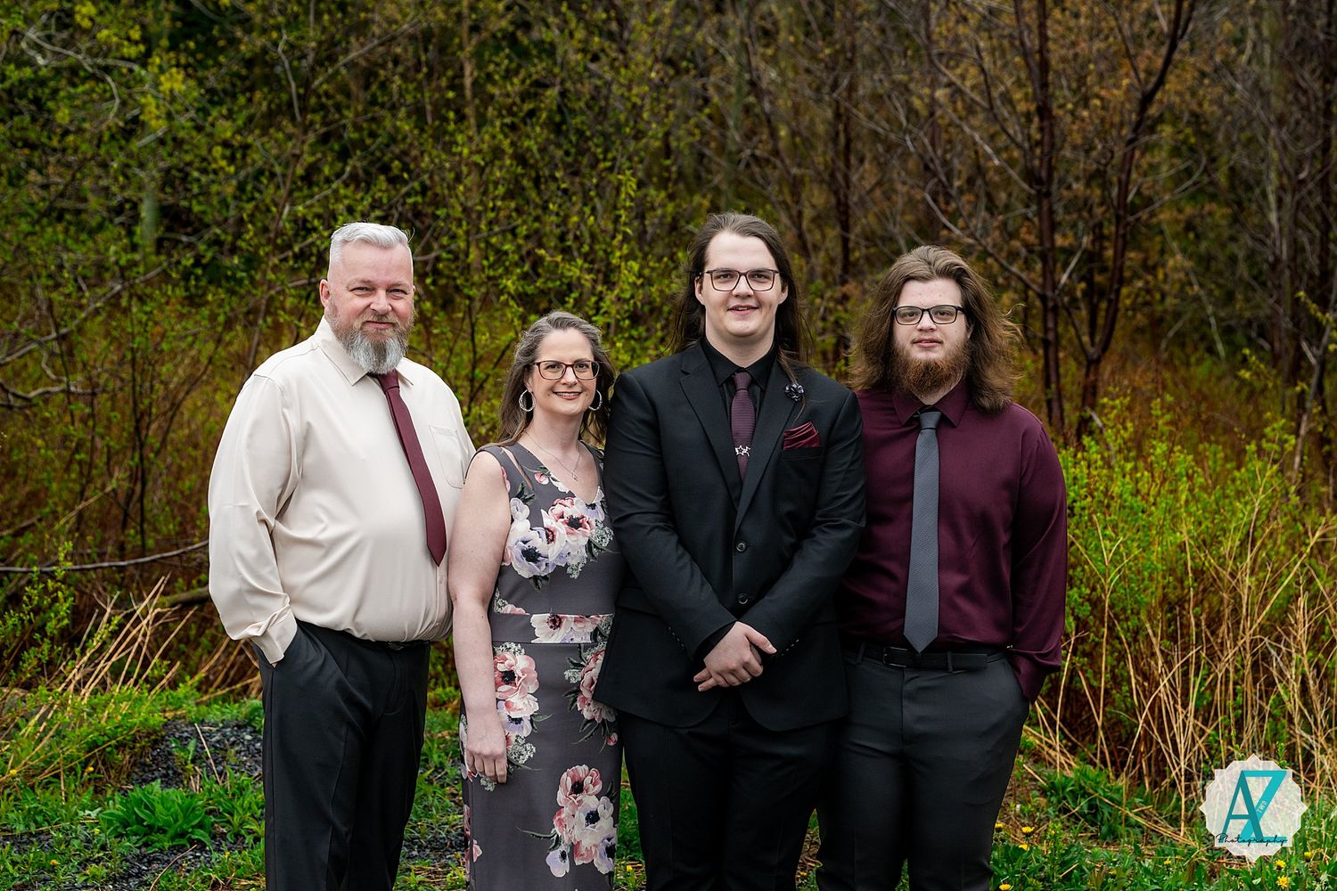 A group of four people standing together outdoors in formal attire against a natural green background.