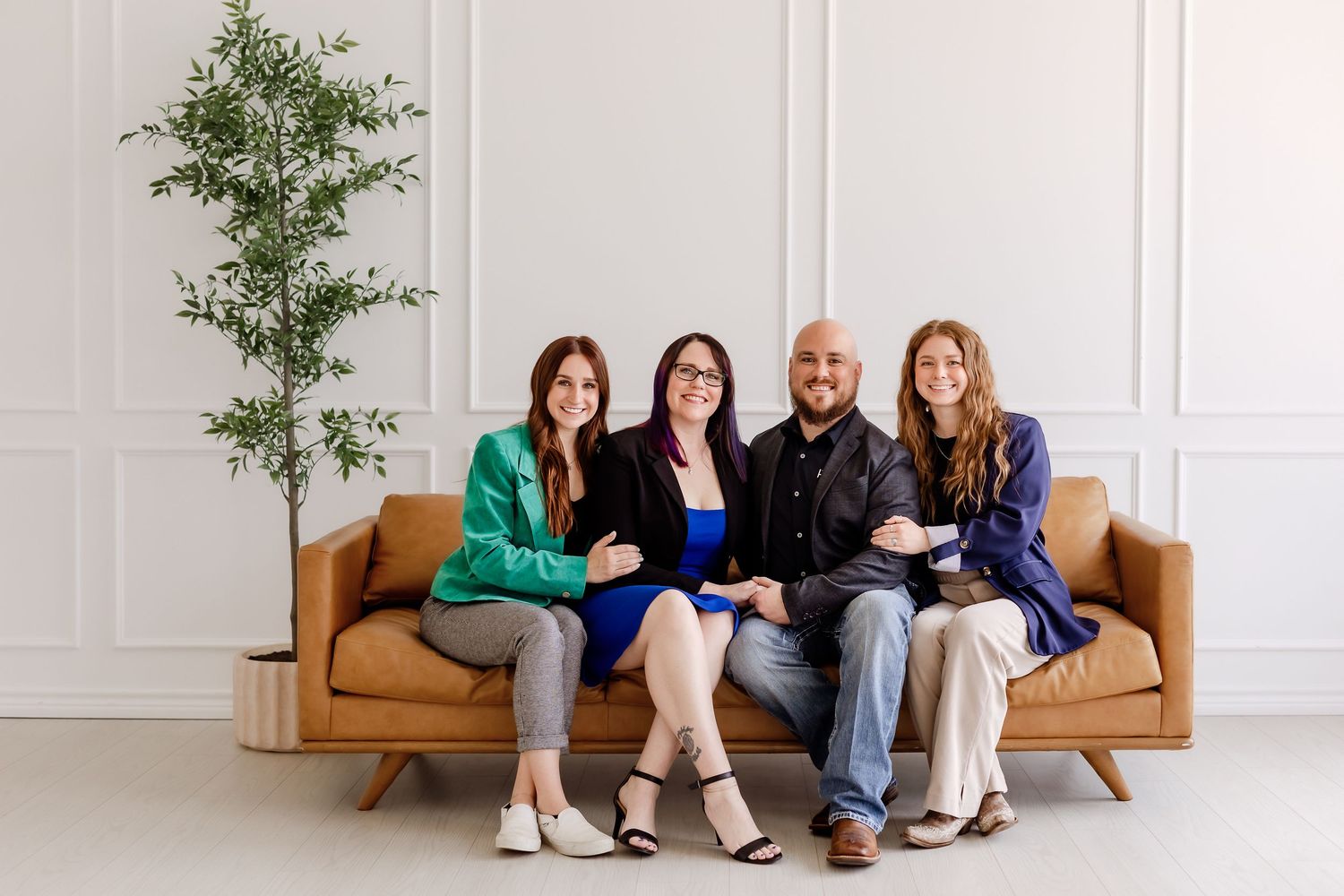 A group sits together on a tan leather couch in a bright minimalist room with a potted plant.
