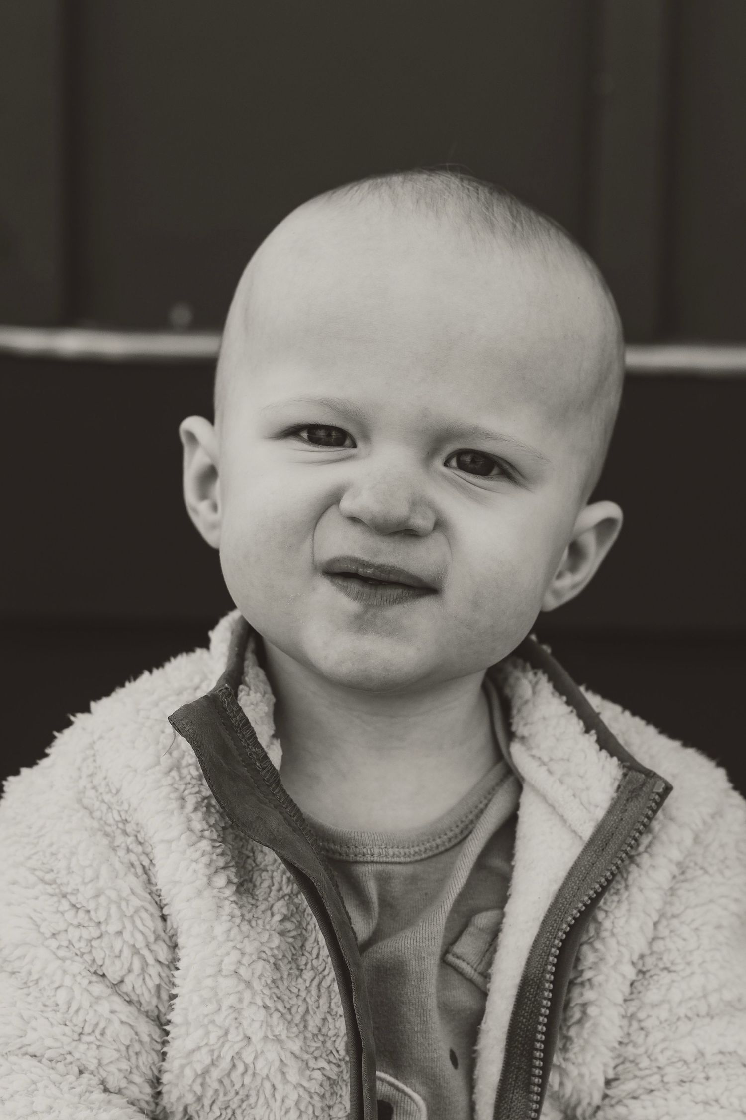 Black and white portrait of a baby wearing a cozy fleece jacket making a playful expression.