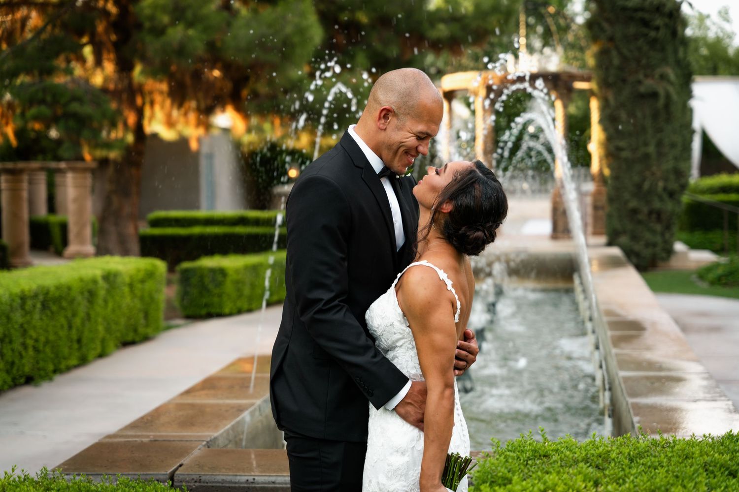 A couple shares a romantic moment near a garden fountain in an elegant outdoor wedding setting.