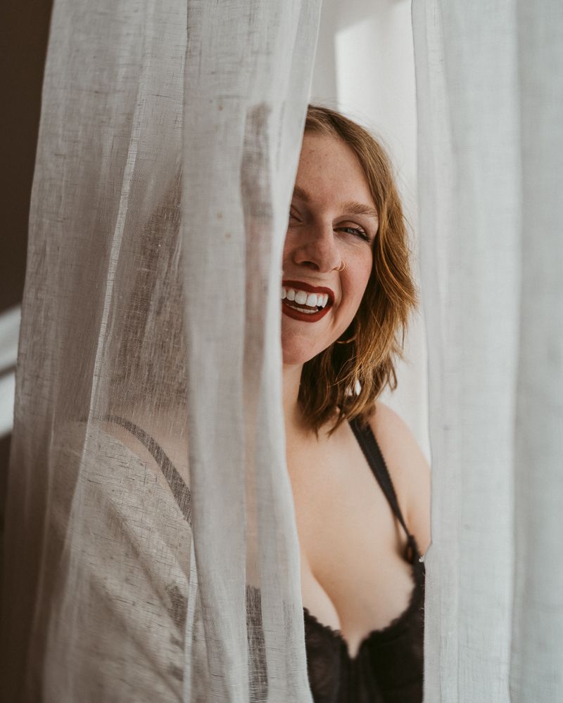 A joyful candid moment captured through sheer white curtains in natural window light.