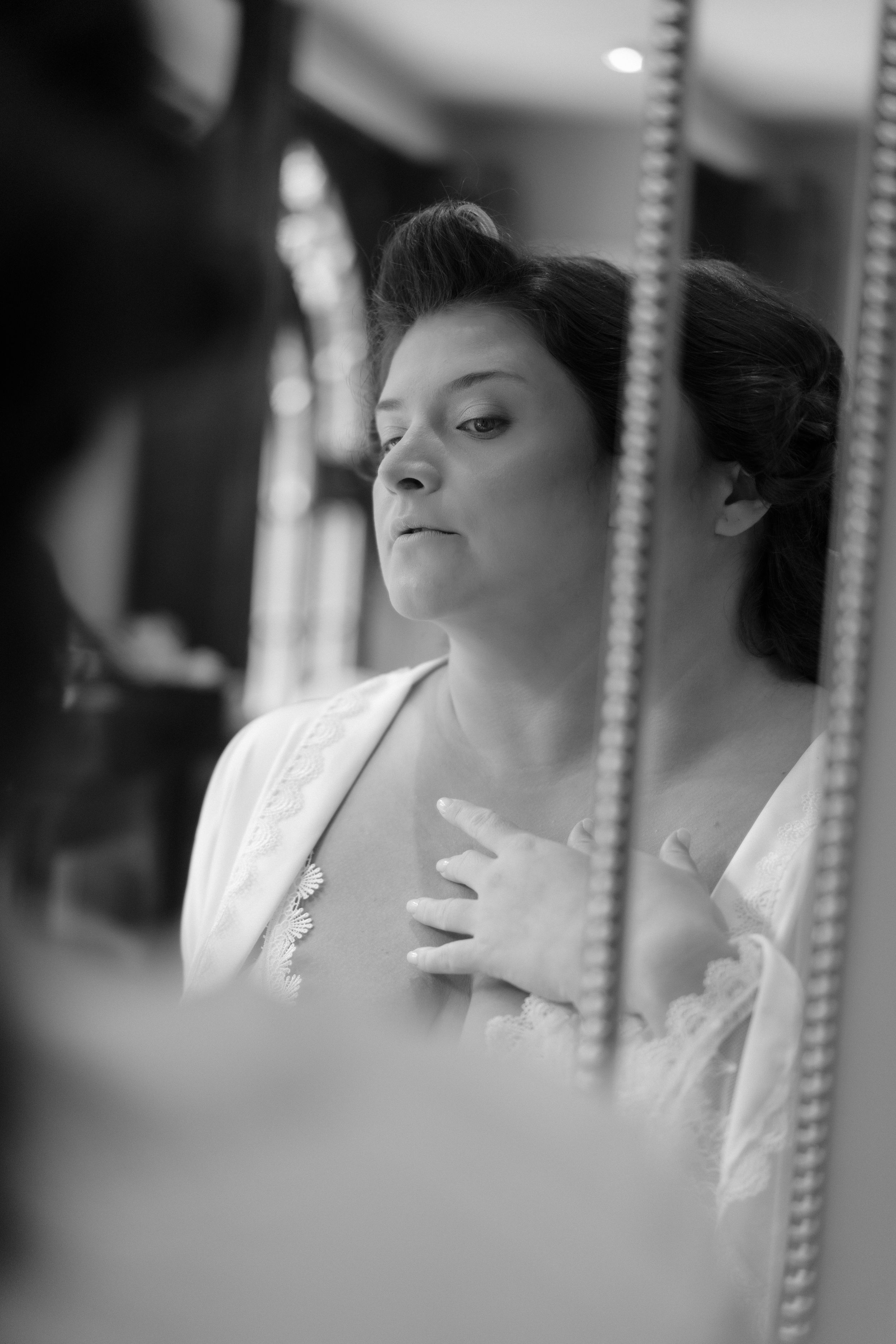 Black and white portrait through a vintage mirror reflection showing bridal preparation.