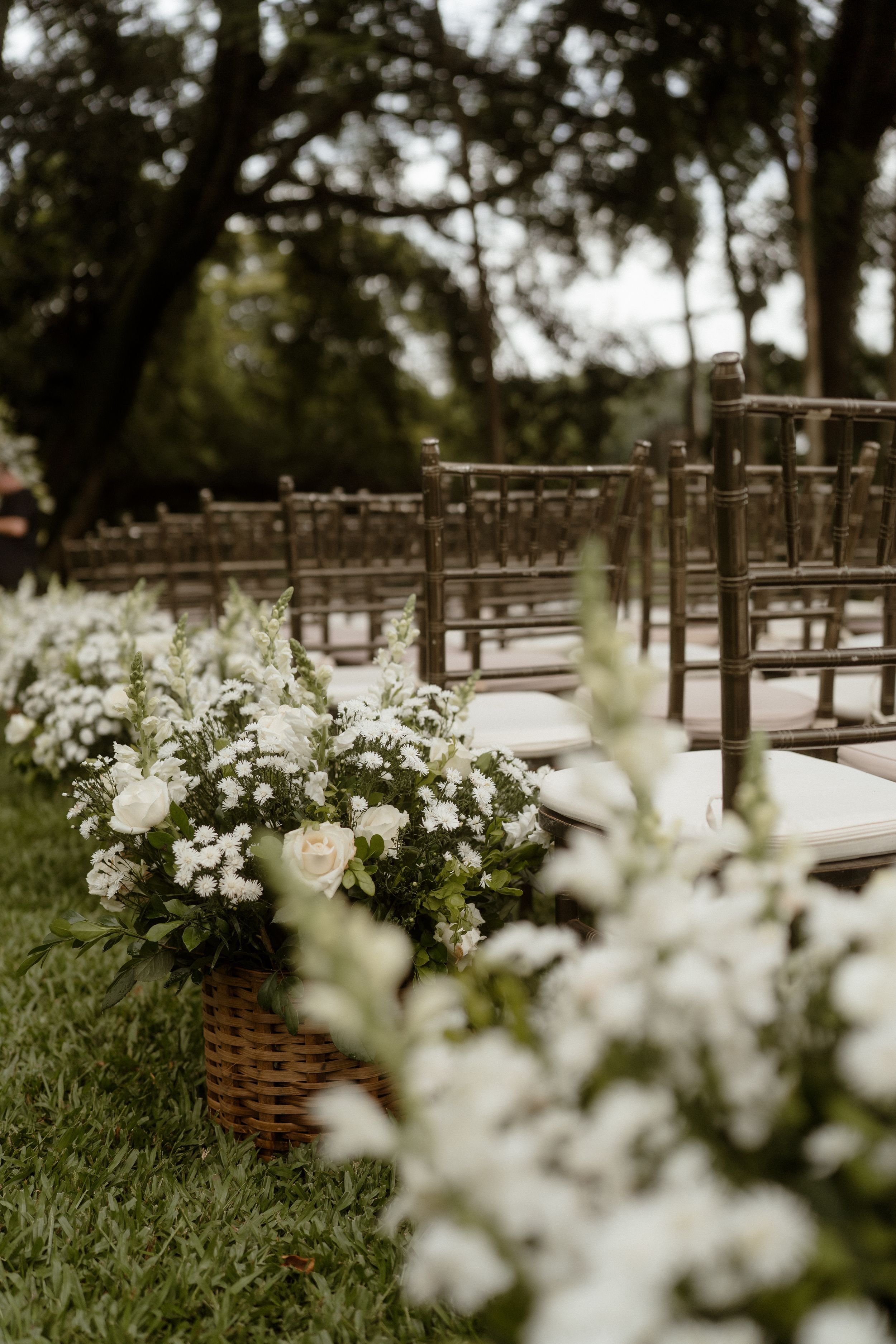 Outdoor wedding ceremony setup with wooden chairs and white floral arrangements along the aisle.