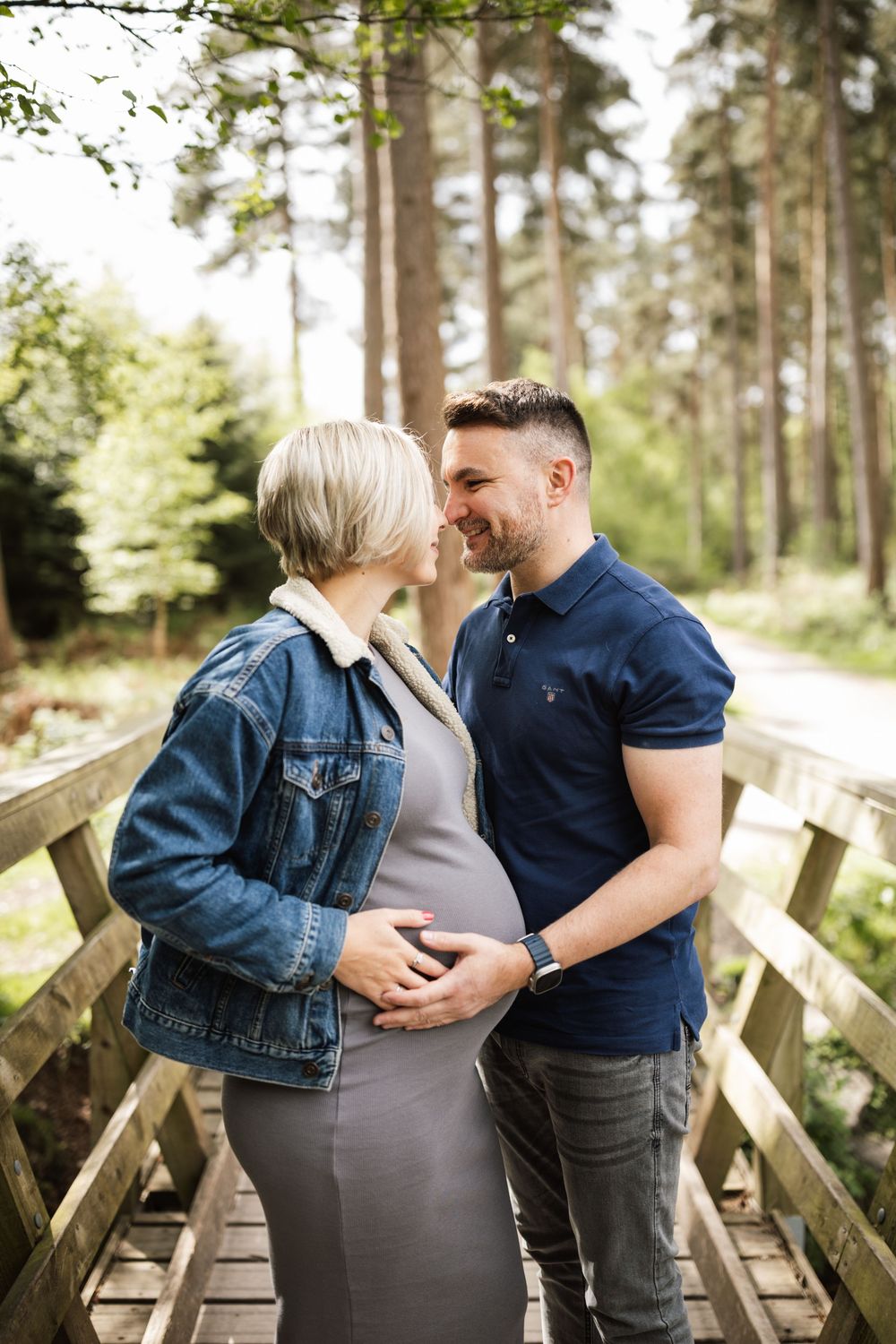 A couple share an intimate moment on a wooden footbridge surrounded by tall pine trees.