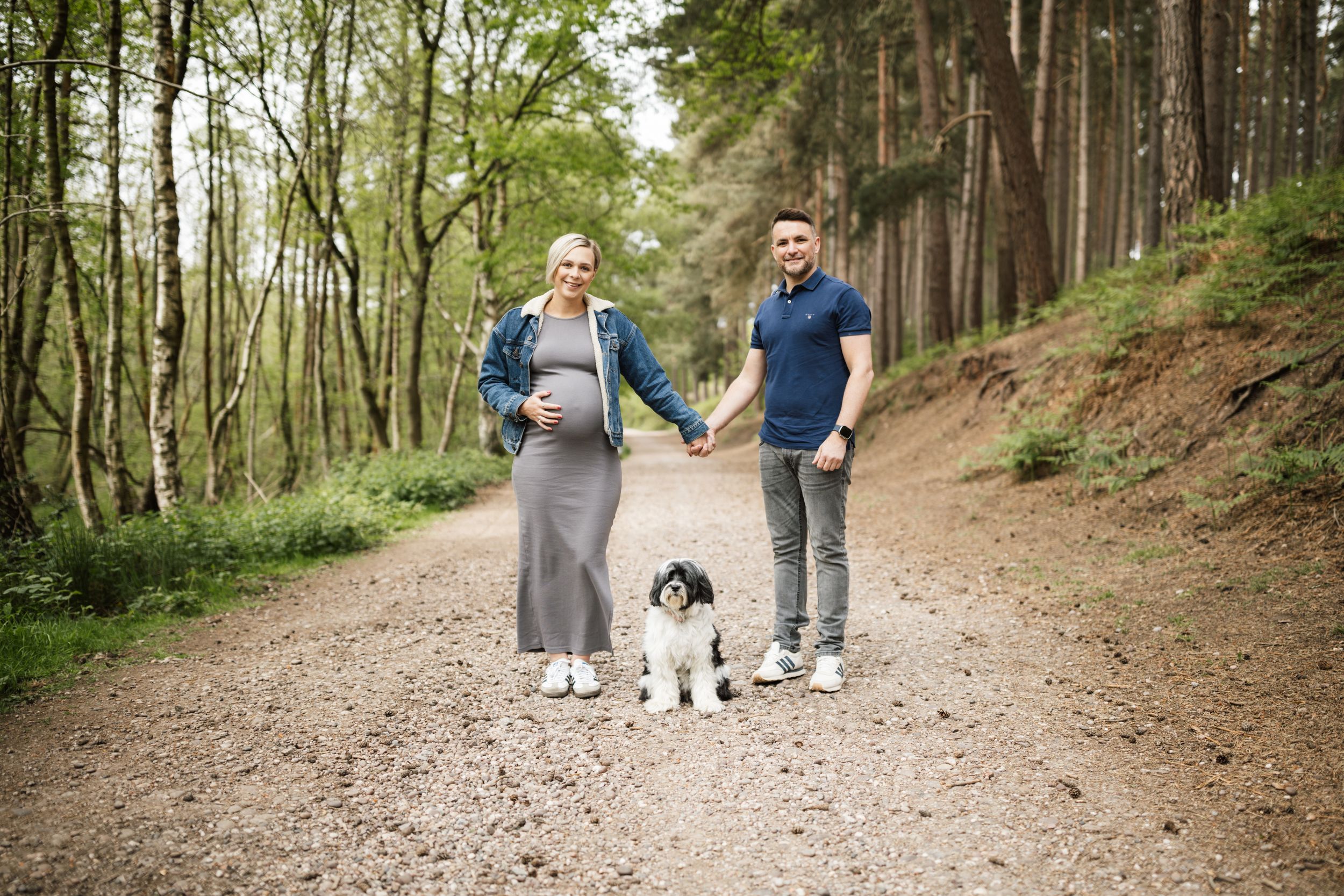 A couple walks their black and white dog along a scenic forest trail on a spring day.