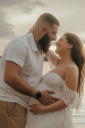 A couple embraces in a romantic sunset moment on the beach, with the bride wearing a lace off-shoulder dress.