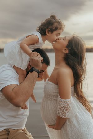 A candid family moment at sunset by the water captured in warm tones with soft lighting and delicate white lace details.