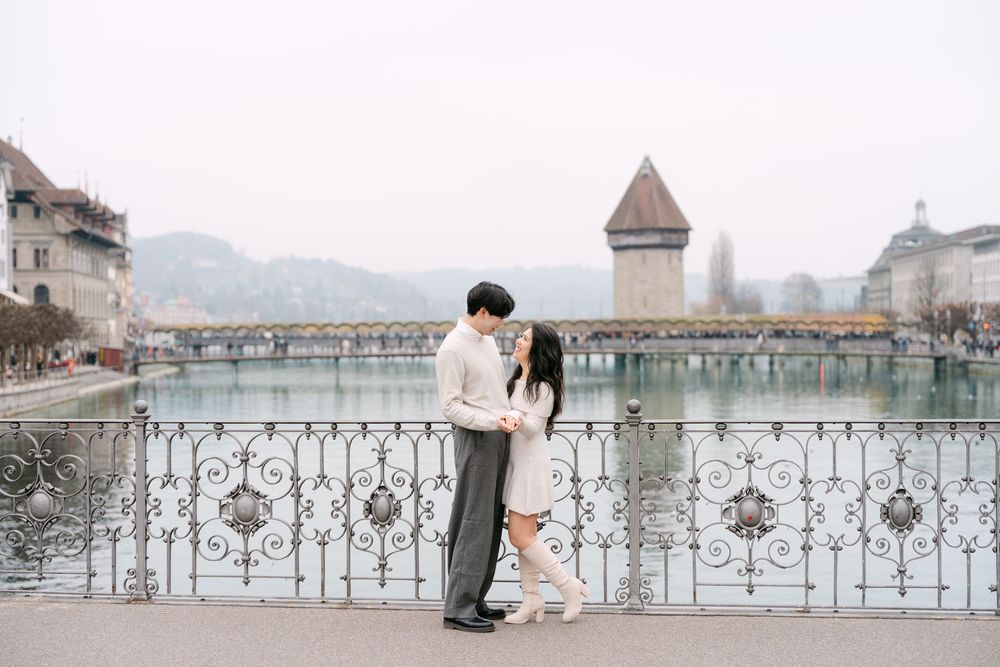 A couple embraces on an ornate bridge overlooking the Chapel Bridge and Water Tower in Lucerne, Switzerland.