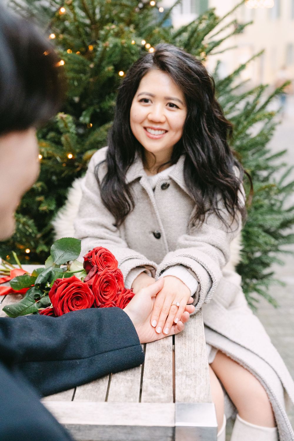 A couple shares a tender moment near a decorated Christmas tree with red roses.