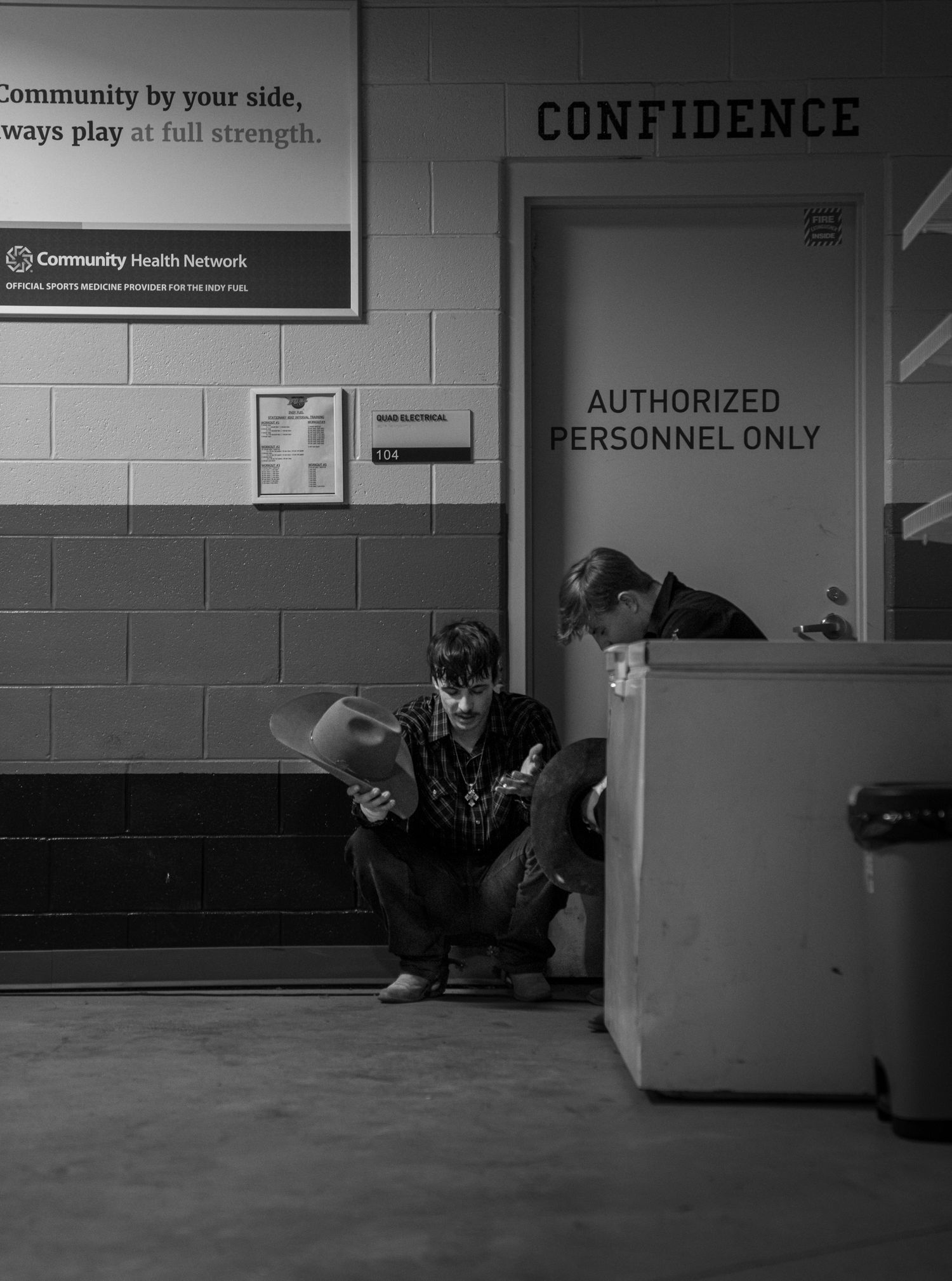 Black and white candid photo of two men praying before riding bulls in a rodeo. Gritty, documentary-style composition.