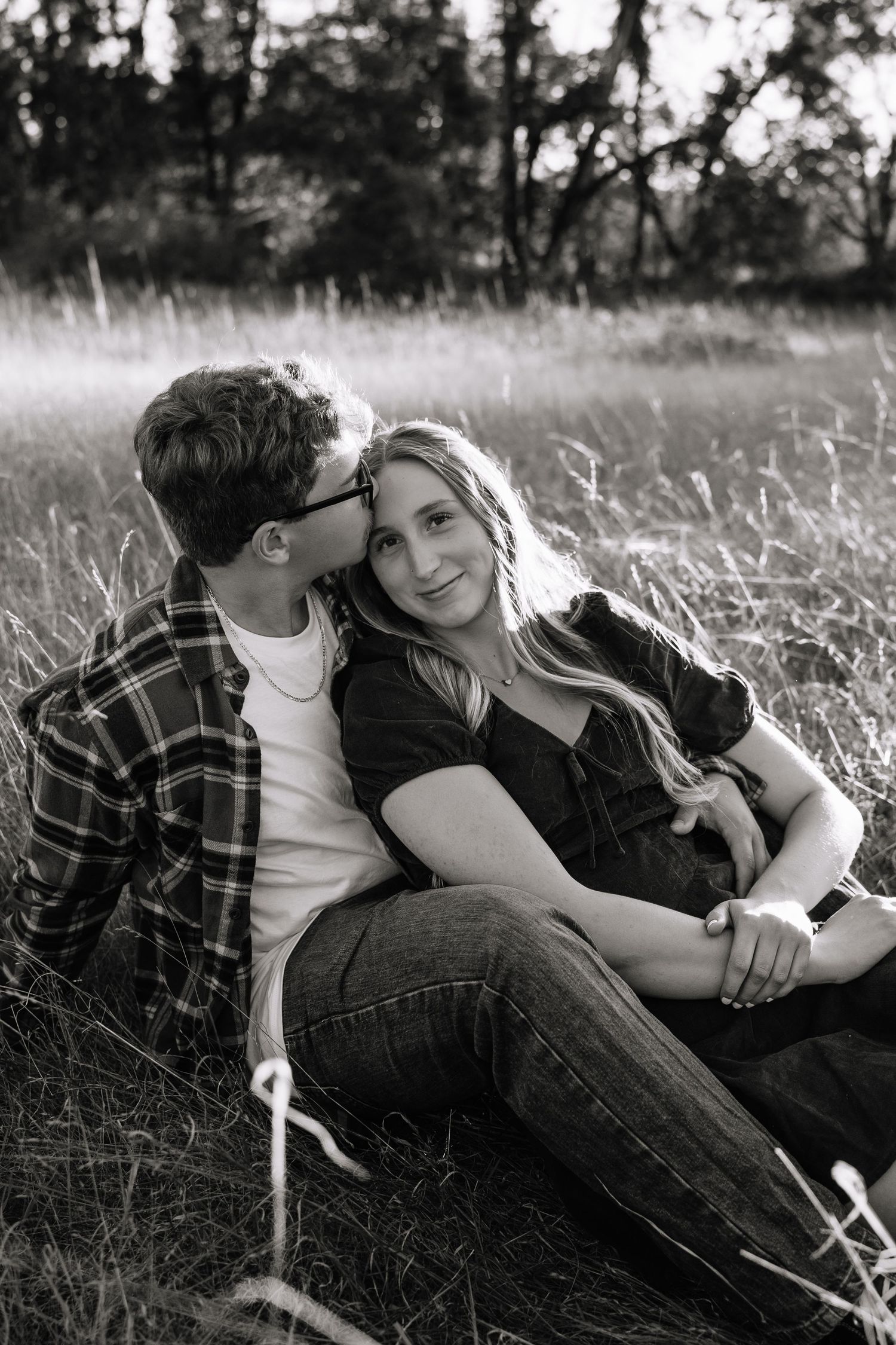 A black and white photo sequence of a couple cuddling in tall grass during an engagement shoot.