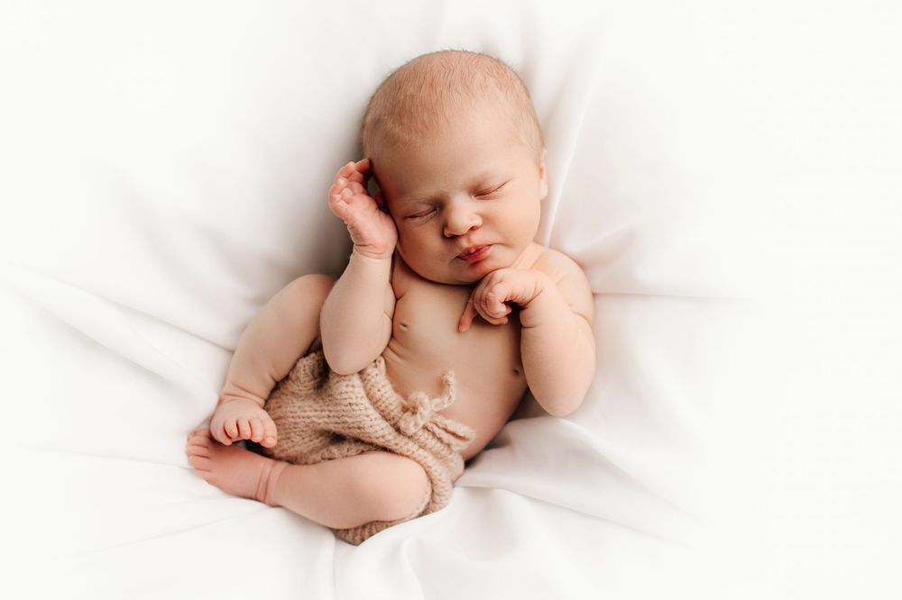Newborn sleeping peacefully in soft white setting.