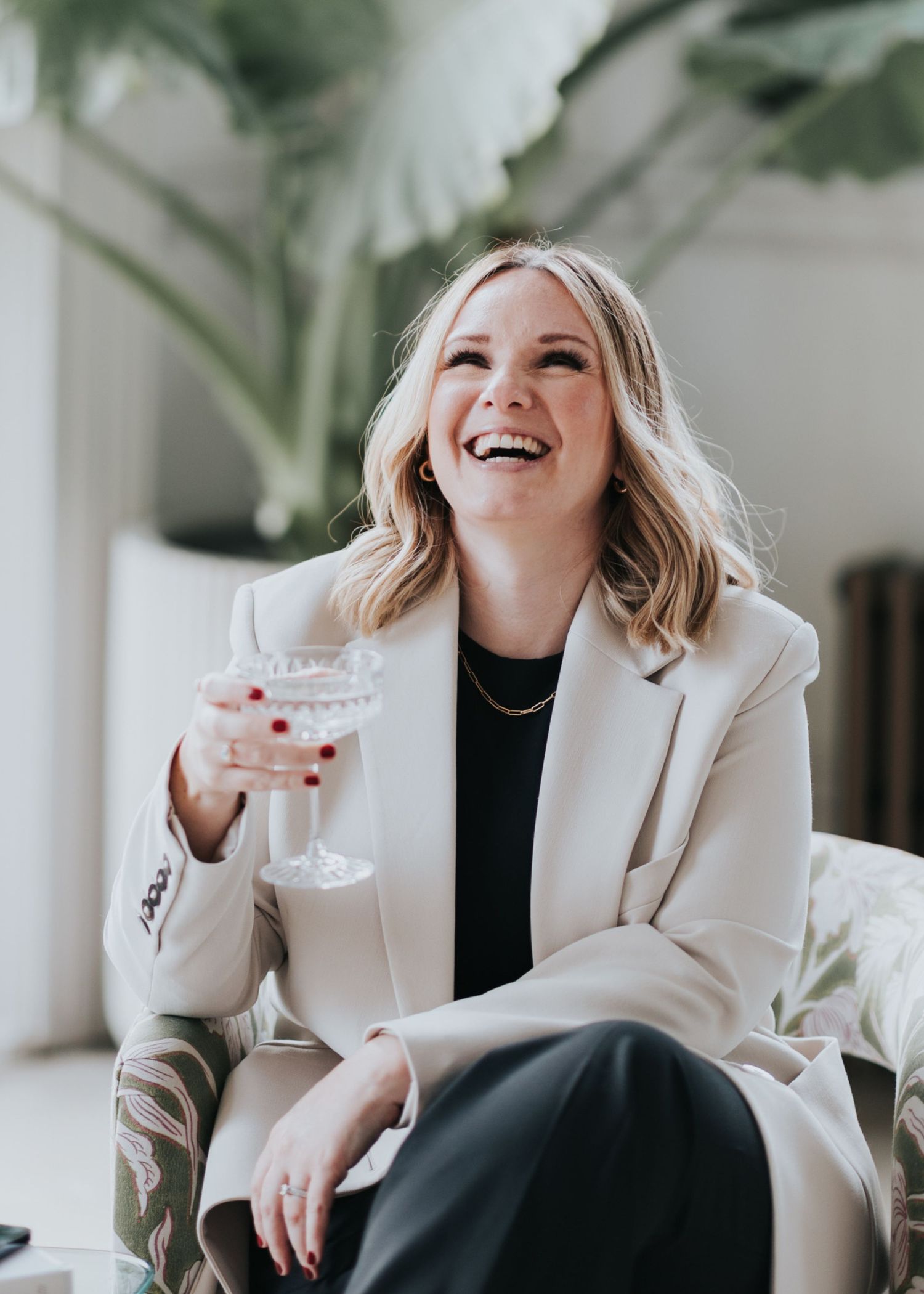 Professional lifestyle photo of someone in a cream blazer and black top laughing joyfully while seated.