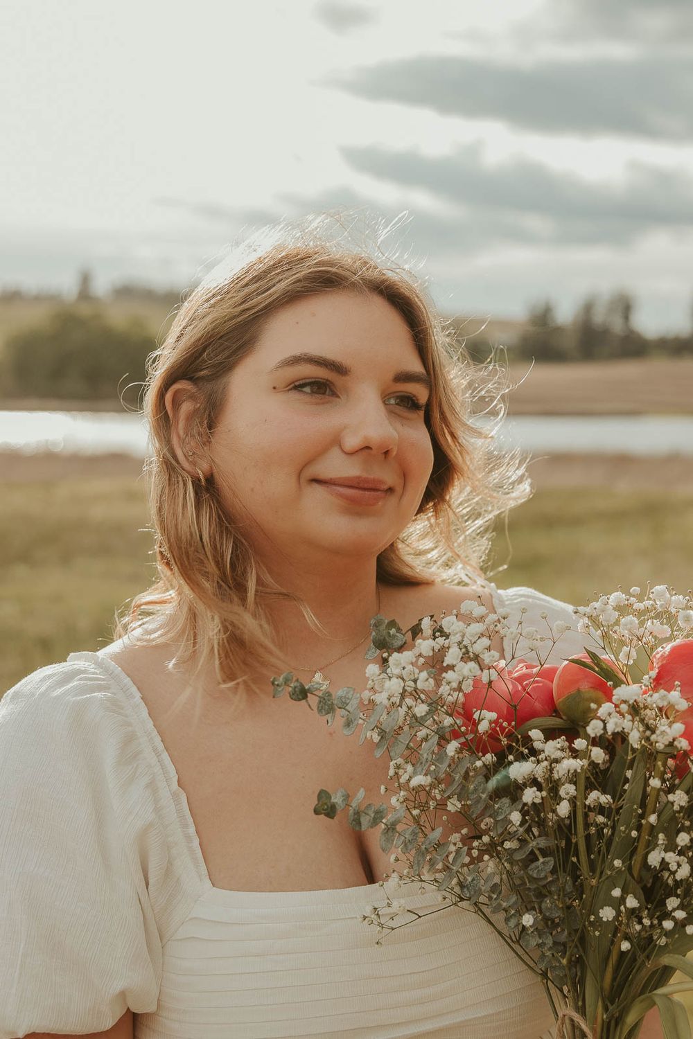 Close-up of smiling senior from Davenport High School holding trader joes flowers during golden hour senior session in field near Spokane
