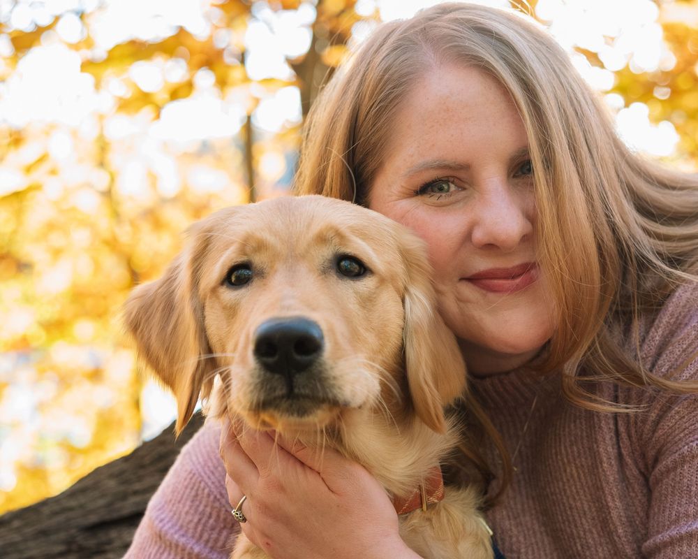 Woman holding golden retriever in fall foliage — warm outdoor lifestyle portrait photography