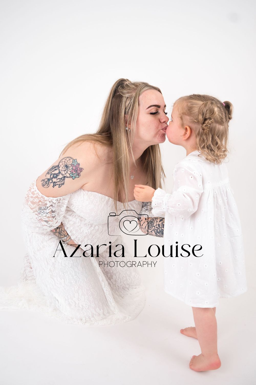 A tender moment captured in white studio photography showing affection between parent and child in matching white outfits.