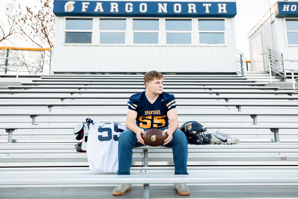 Athlete in jersey sits on Fargo North bleachers with football uniform.