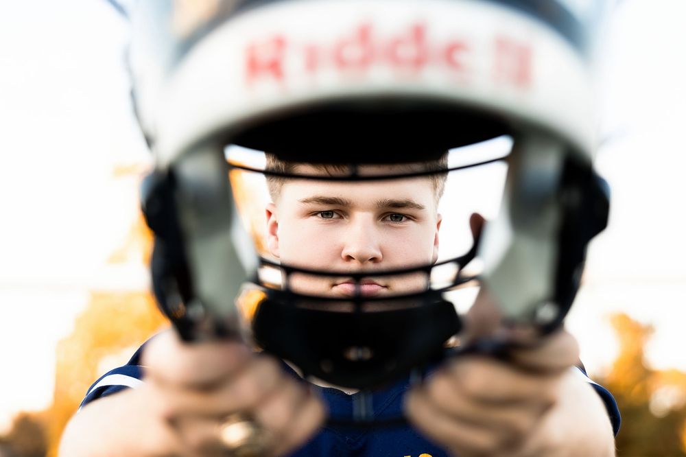 A close-up view of someone wearing a white football helmet with protective face mask in focus.