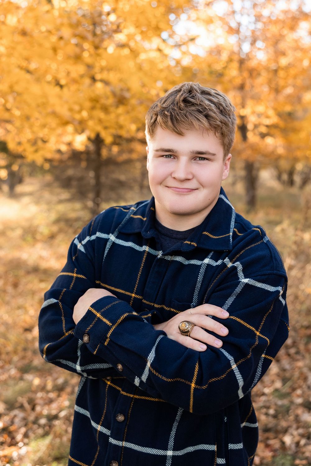A person wearing a navy plaid flannel shirt poses outdoors against vibrant autumn foliage.