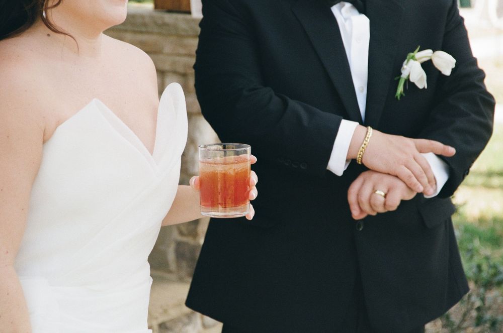 Close-up of couple at wedding with bride in white dress holding cocktail and groom in classic black tuxedo.