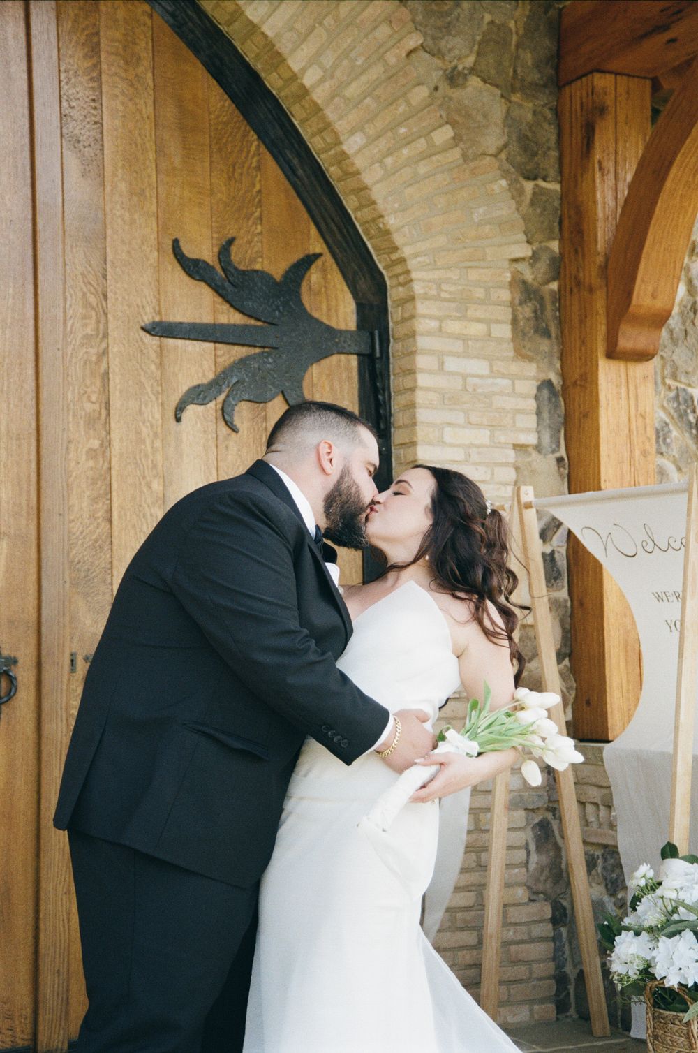 A romantic wedding moment with couple embracing under a rustic brick archway decorated with a metal bird silhouette.