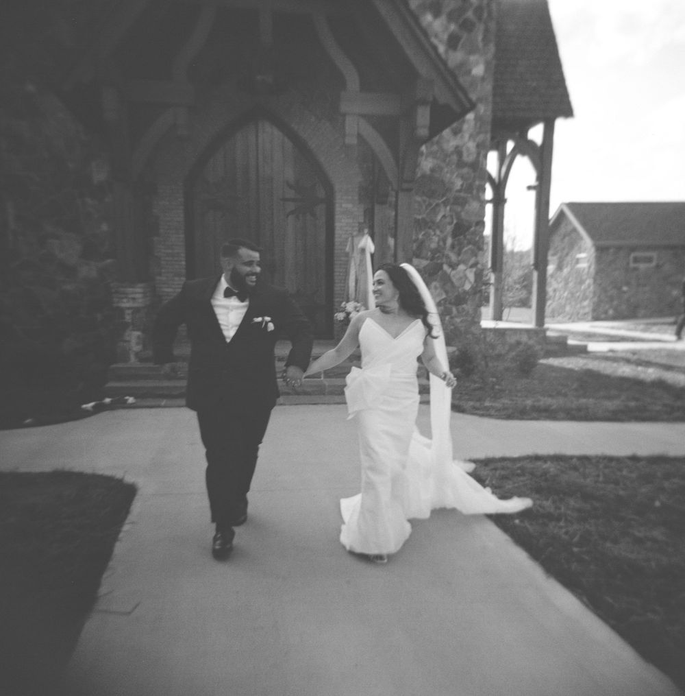 A romantic black and white photograph showing a couple walking together outside a stone church building.