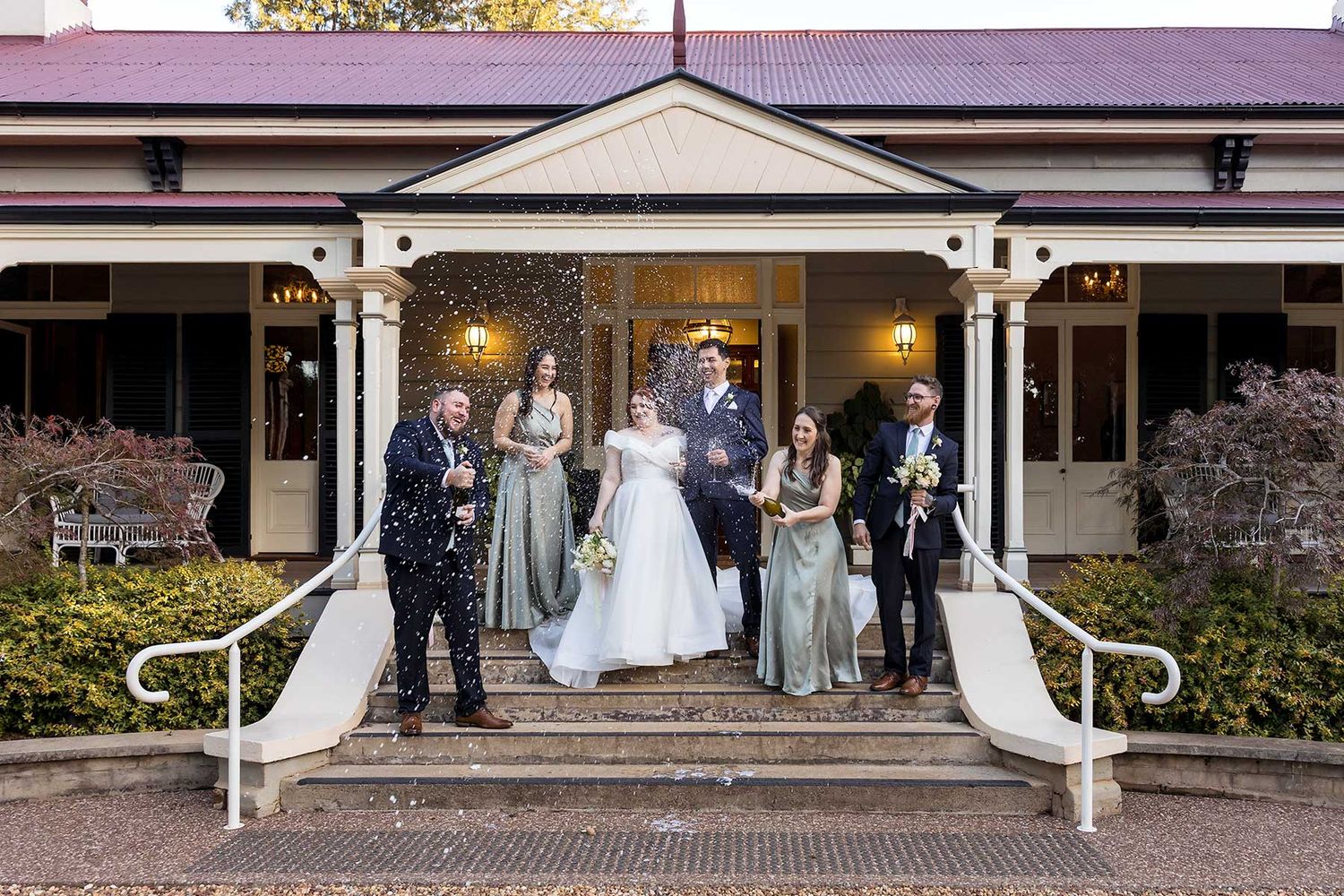 Traditional wedding ceremony participants gather on a brick-paved walkway in front of a columned Southern-style porch entrance at Gabbinbar.