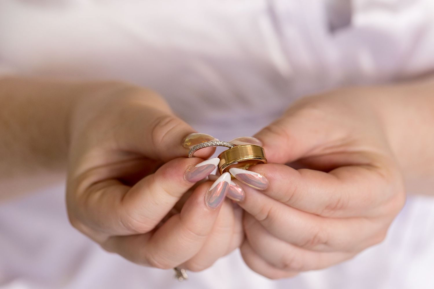 Close-up of a Brides hands holding her Engagement and wedding ring with soft white background.