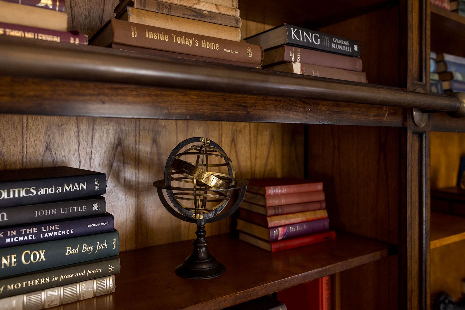 Vintage world globe and classic books displayed on wooden library shelves in warm lighting.