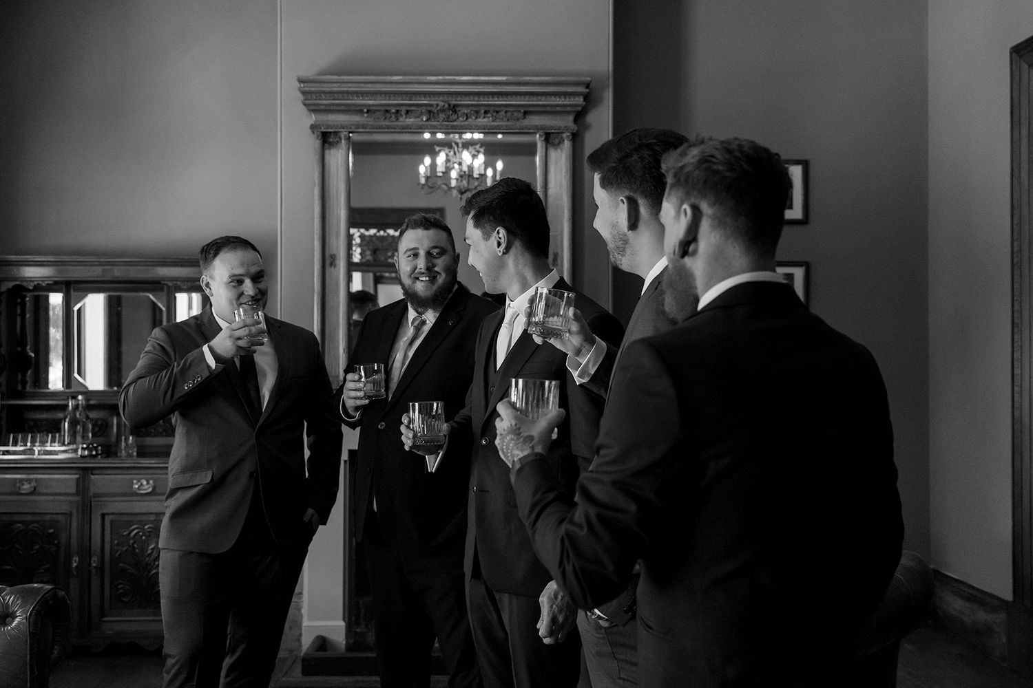 A black and white photograph shows a Groom with his Groomsmen sharing a moment with a glass of whiskey in the Library at Gabbinbar Homestead