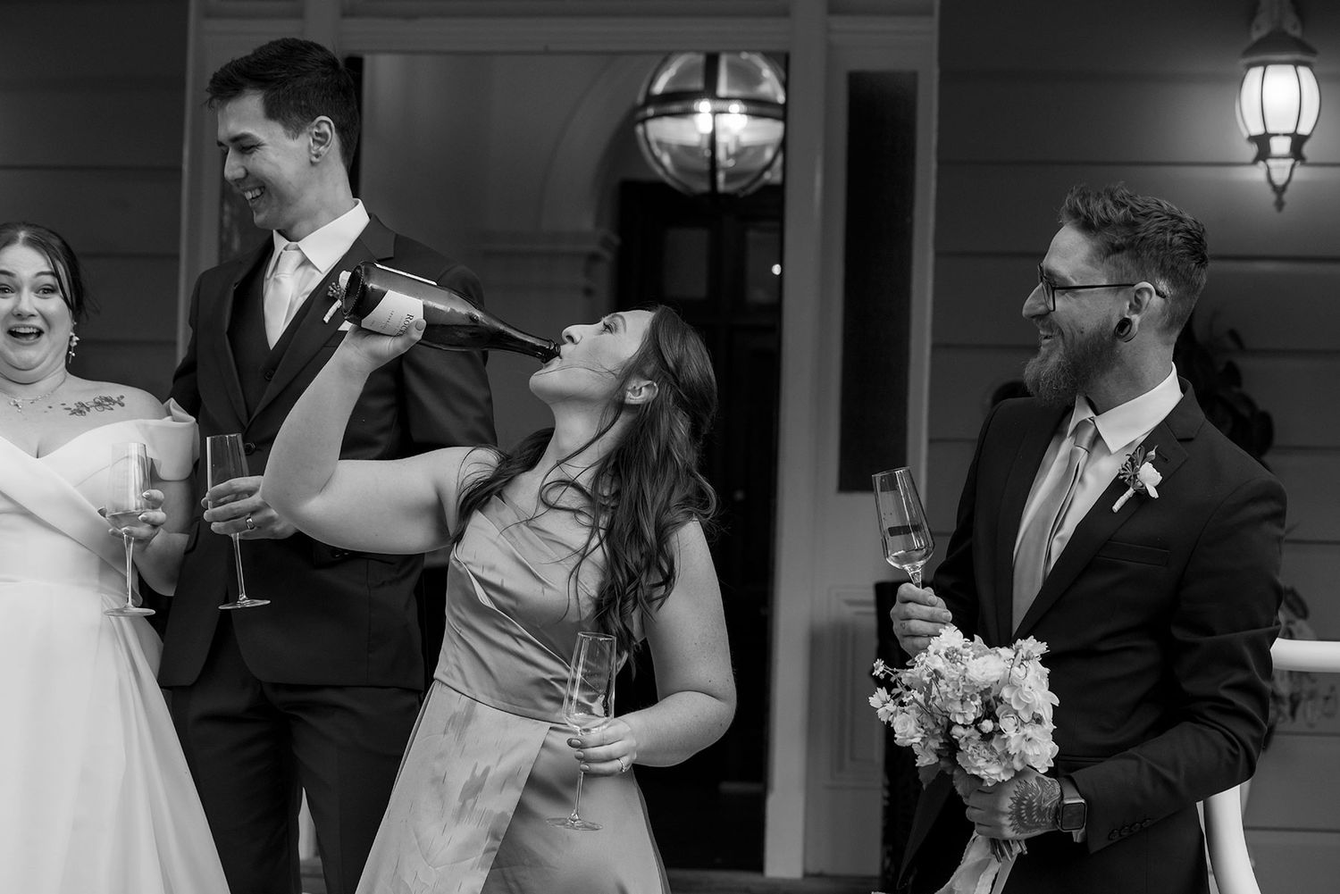 A candid black and white photo of people laughing together at a wedding celebration outdoors.