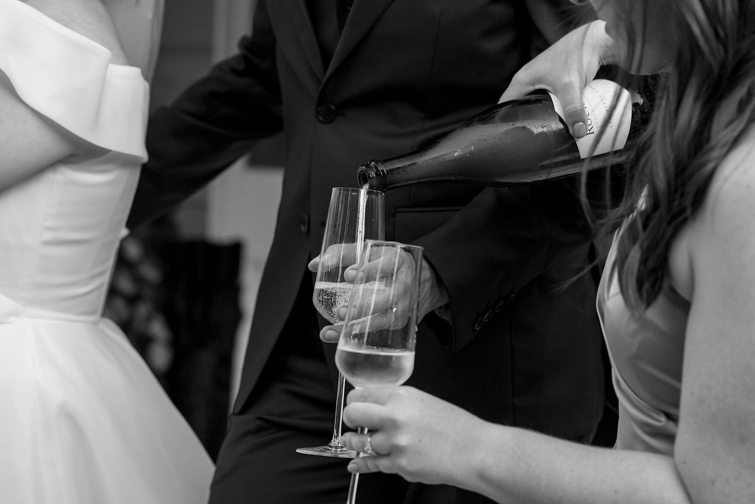 Black and white photo showing hands pouring champagne into a glass at an elegant event.