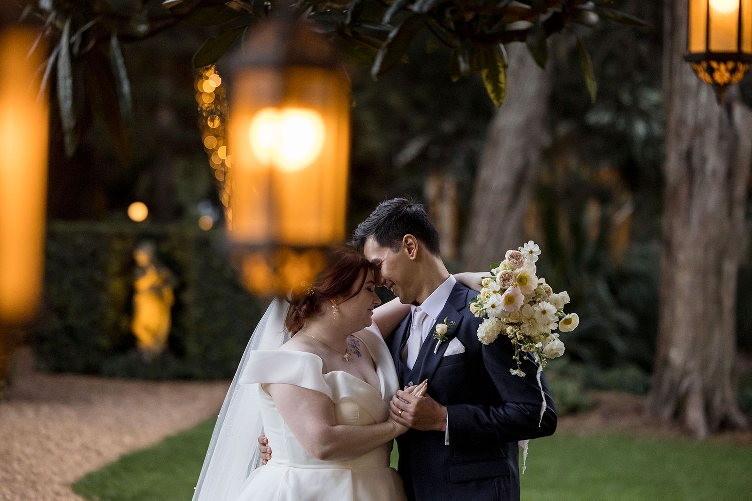 A Bride and Groom share an intimate moment on a gravel path surrounded by lush greenery and golden evening lighting at Gabbinbar Toowoomba.