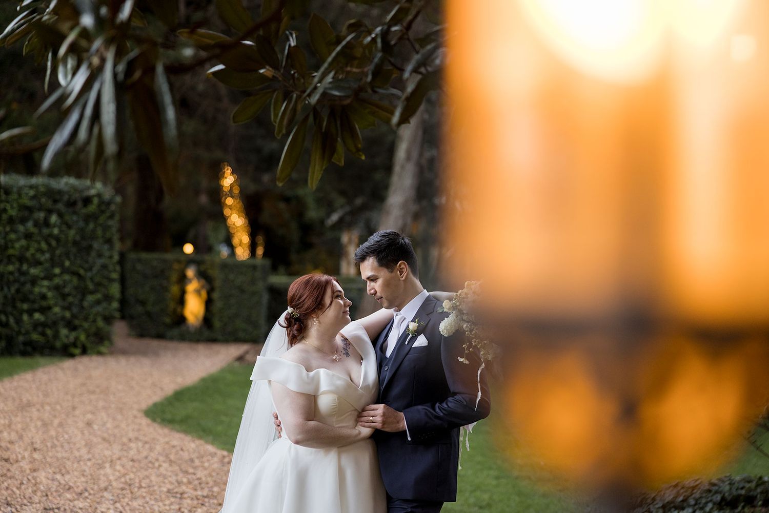 A Bride and Groom share an intimate moment on a gravel path surrounded by lush greenery and golden evening lighting at Gabbinbar Toowoomba.