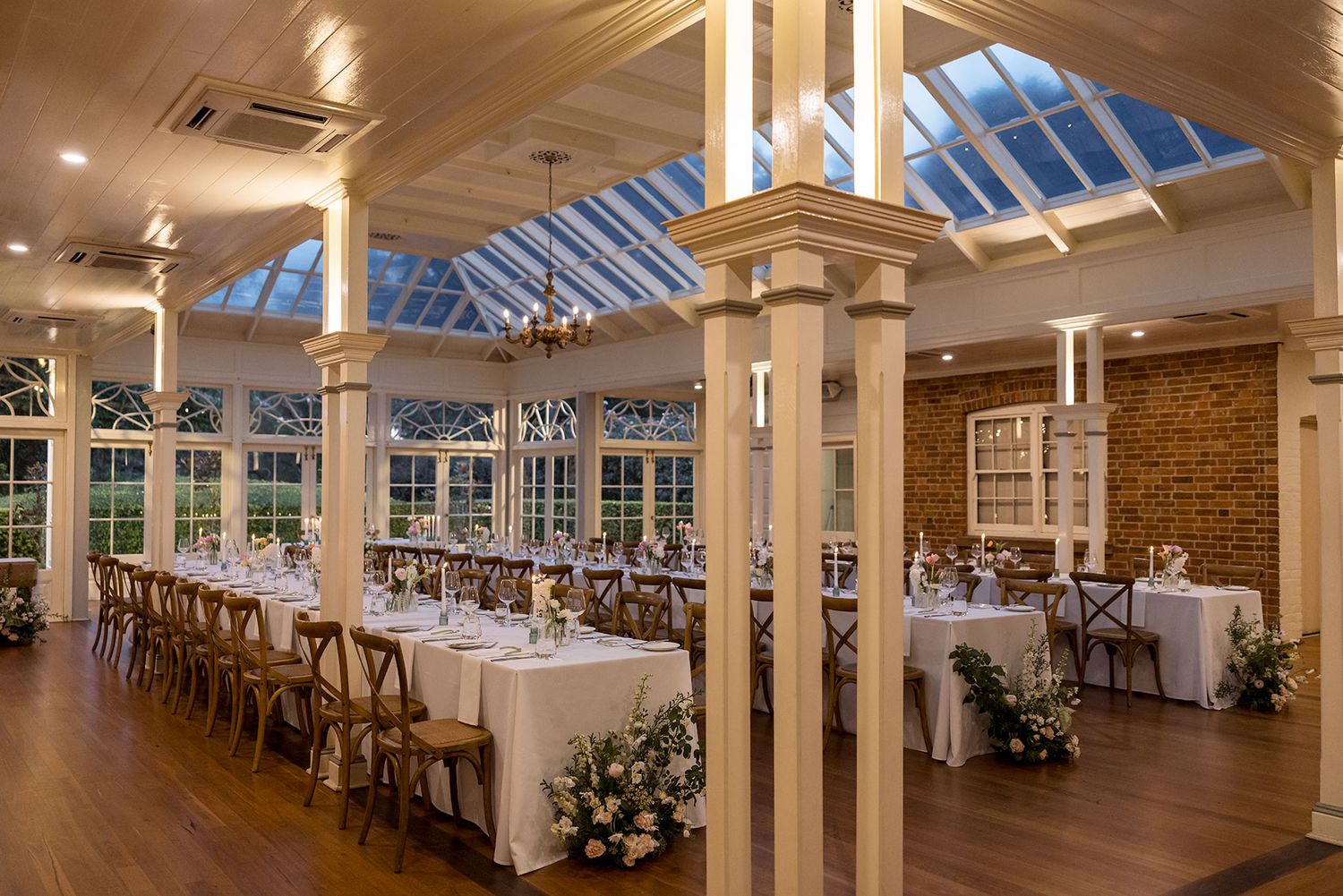 Elegant banquet hall with skylight windows, wooden floors, white tablecloths, and exposed brick walls glowing in warm lighting at Gabbinbar.
