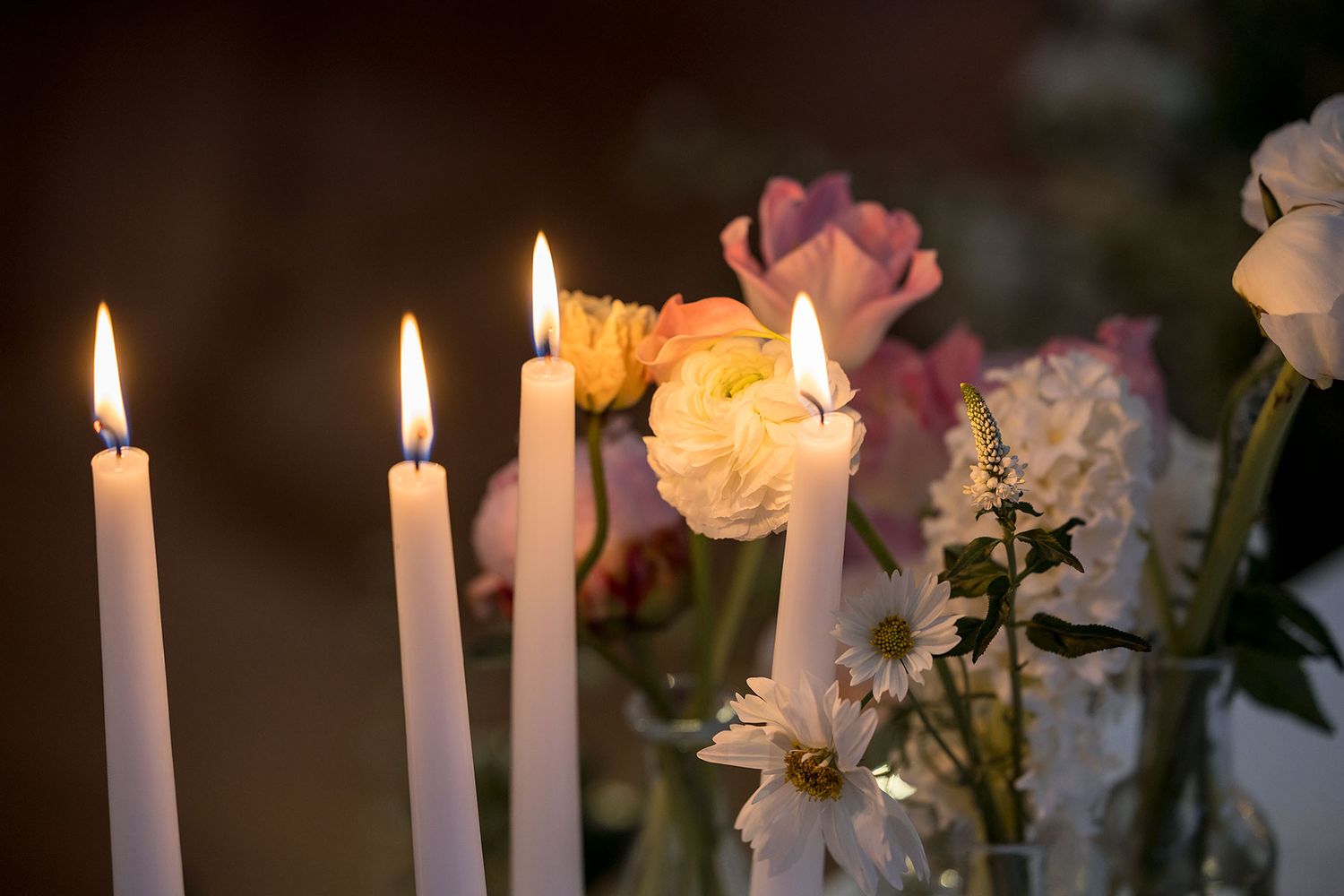 White candles burning beside delicate pink and yellow flowers in a romantic candlelit setting in the Conservatory at Gabbinbar Homestead.