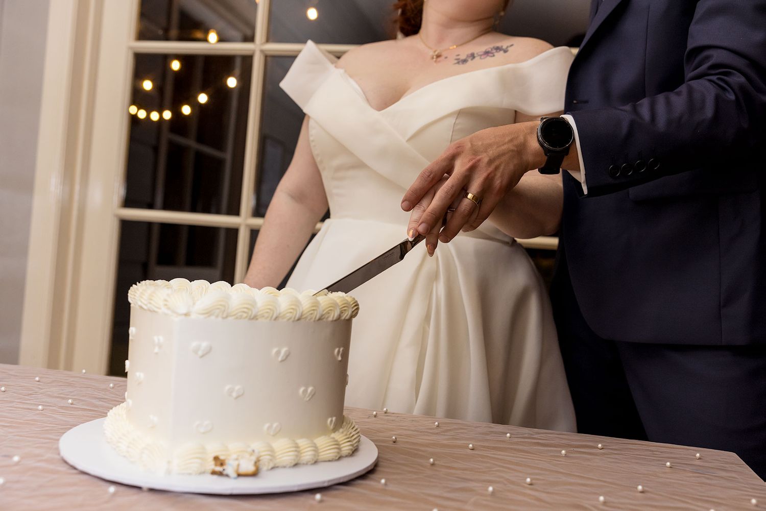 A couple cuts into a simple white wedding cake with pearl decorations during an evening wedding reception at Gabbinbar Homestead.