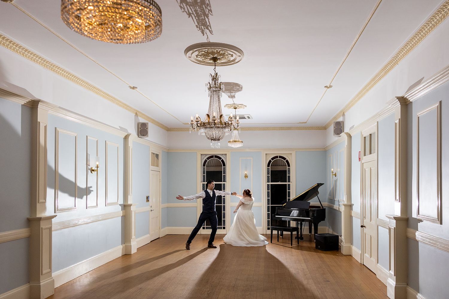 Elegant ballroom at Gabbinbar with ornate chandeliers, white wainscoting, and a grand piano with the Bride and Groom sharing their 1st dance