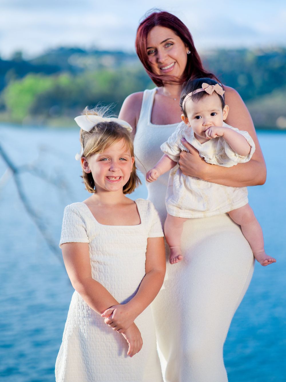 Mother and children in white outfits pose for a portrait by the water.
