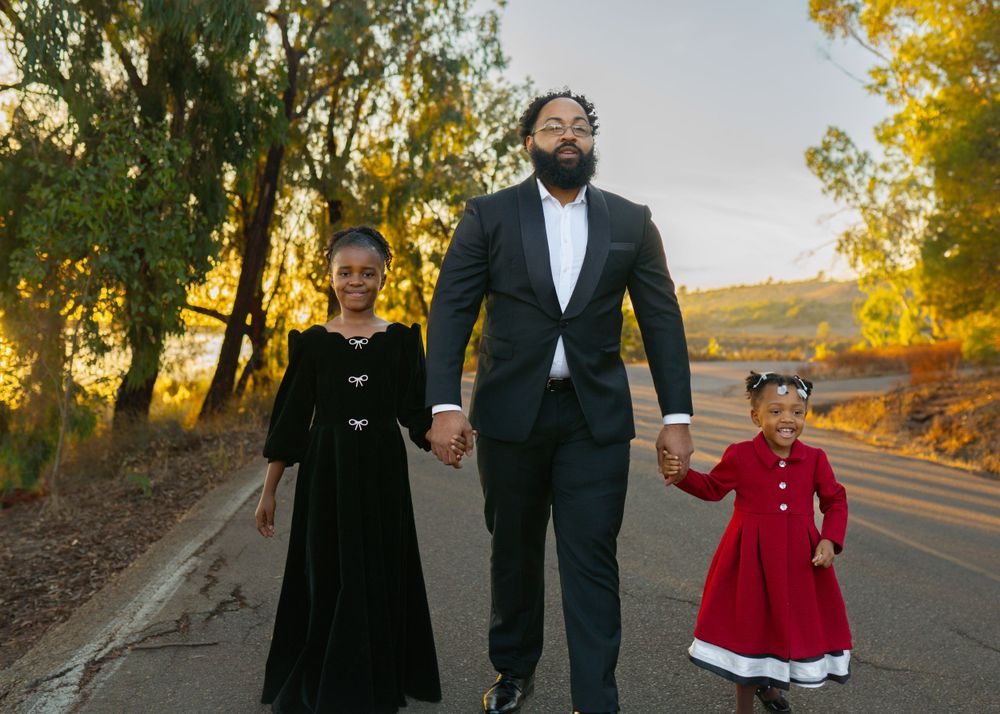 Family walking on path at sunset, with children in formal black and red dresses.