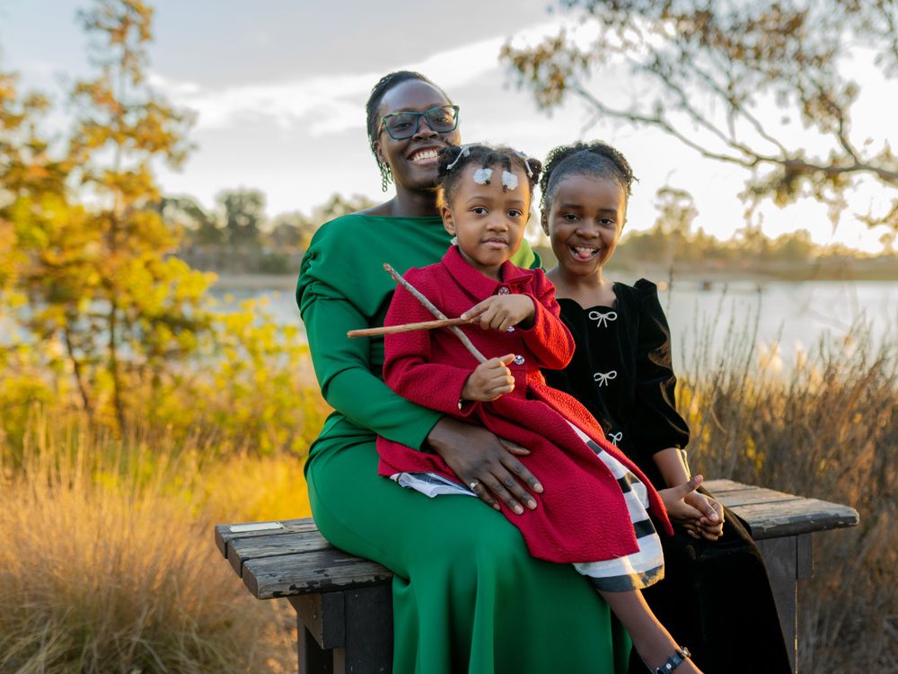 Family in formal attire sitting together on bench at sunset by lake.