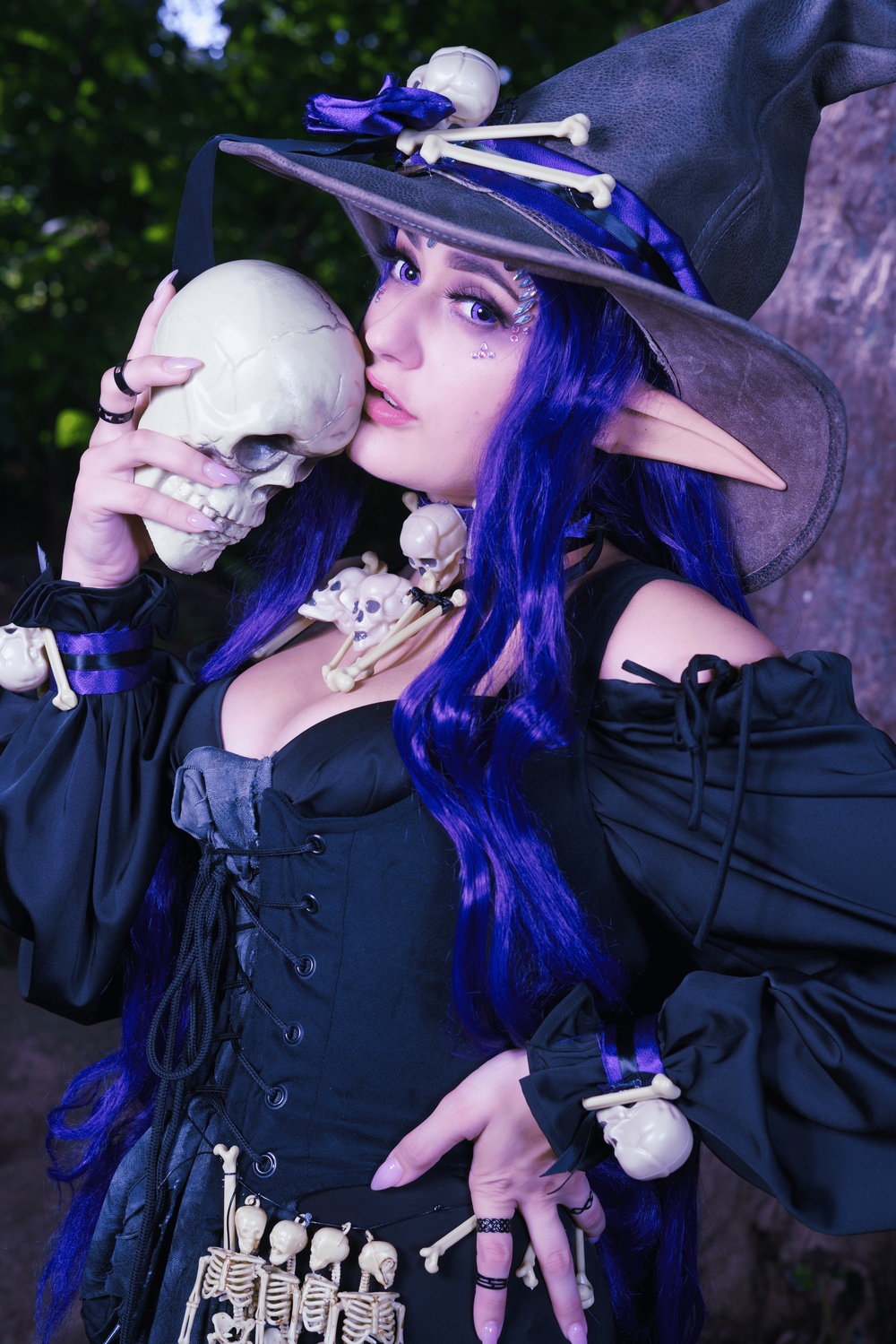 Piexv Cosplay in a Necromantic Witch outfit, giving a tender kiss to a former victim's skull while adorned in bones