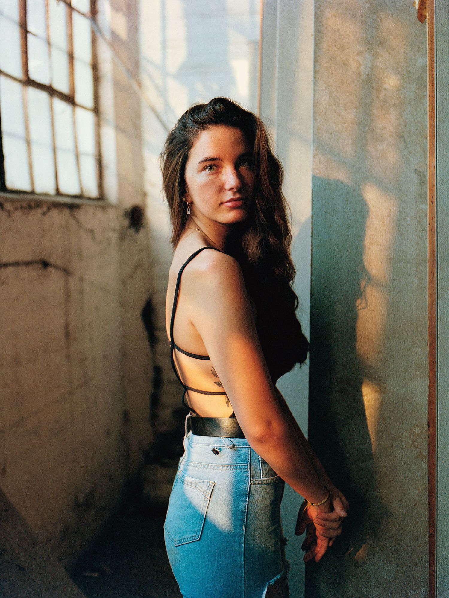 Artistic portrait in abandoned warehouse with dramatic window lighting.