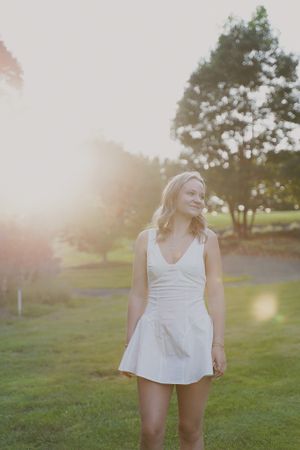 Summer portrait in white dress standing on grass during golden hour sunset.