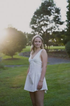 Portrait session in a white sundress on grassy lawn during sunset.