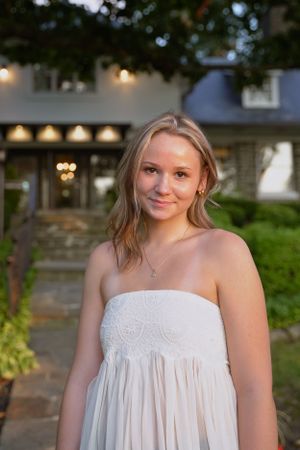 Evening portrait in white lace dress with building and outdoor lighting in background.
