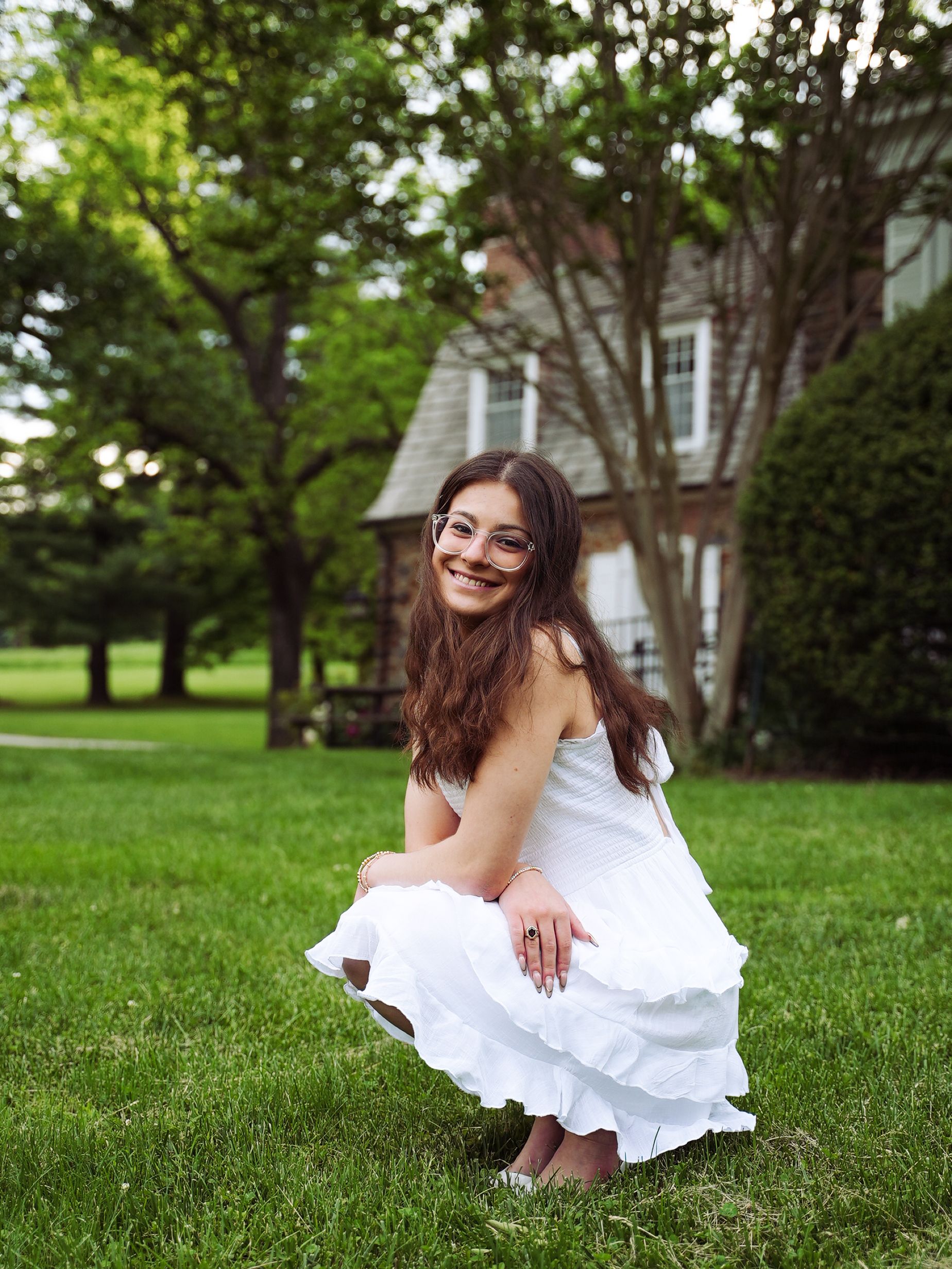 A person in a white dress sits gracefully on lush green grass while enjoying a sunny summer day outdoors.