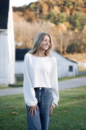 Fashion photo showcasing a white knit sweater and jeans in a rural setting.