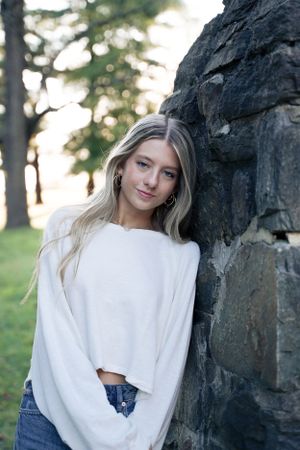 Portrait against a stone wall featuring casual white sweater and denim outfit.